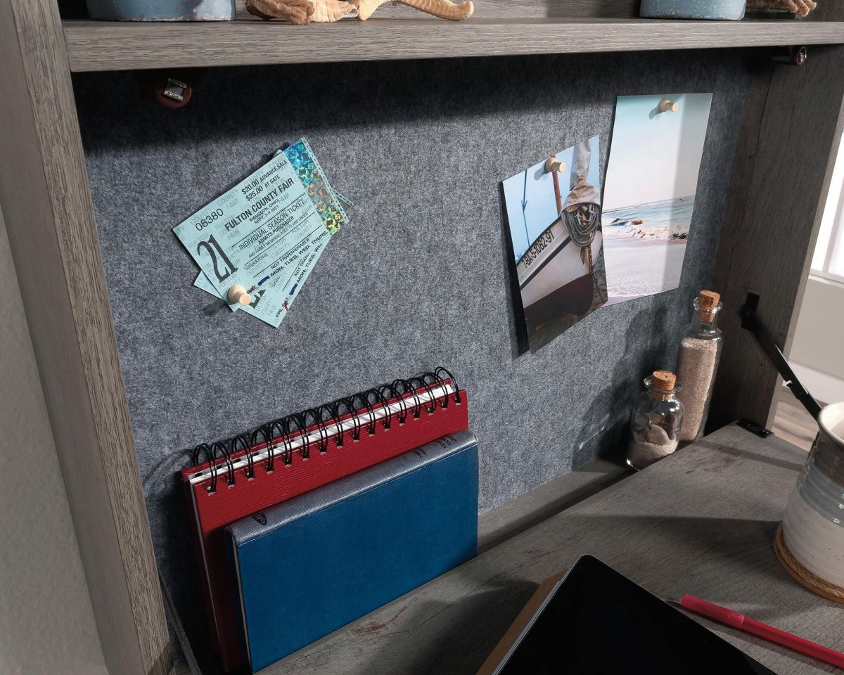 Desk with a felt panel, notebook, and photos on a wooden shelf.