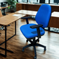 Blue office chair in an office setting with desks and computers.