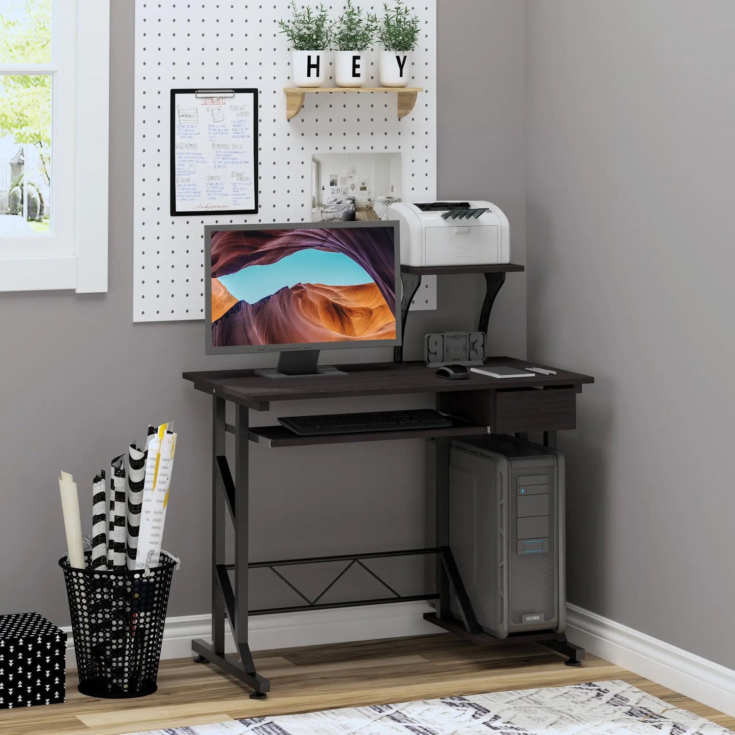 A brown computer desk with a display stand, keyboard tray drawer, and host box shelf. It is set in a room with a wall-mounted shelf above it and a variety of items on and around the desk.