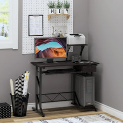 A brown computer desk with a display stand, keyboard tray drawer, and host box shelf. It is set in a room with a wall-mounted shelf above it and a variety of items on and around the desk.