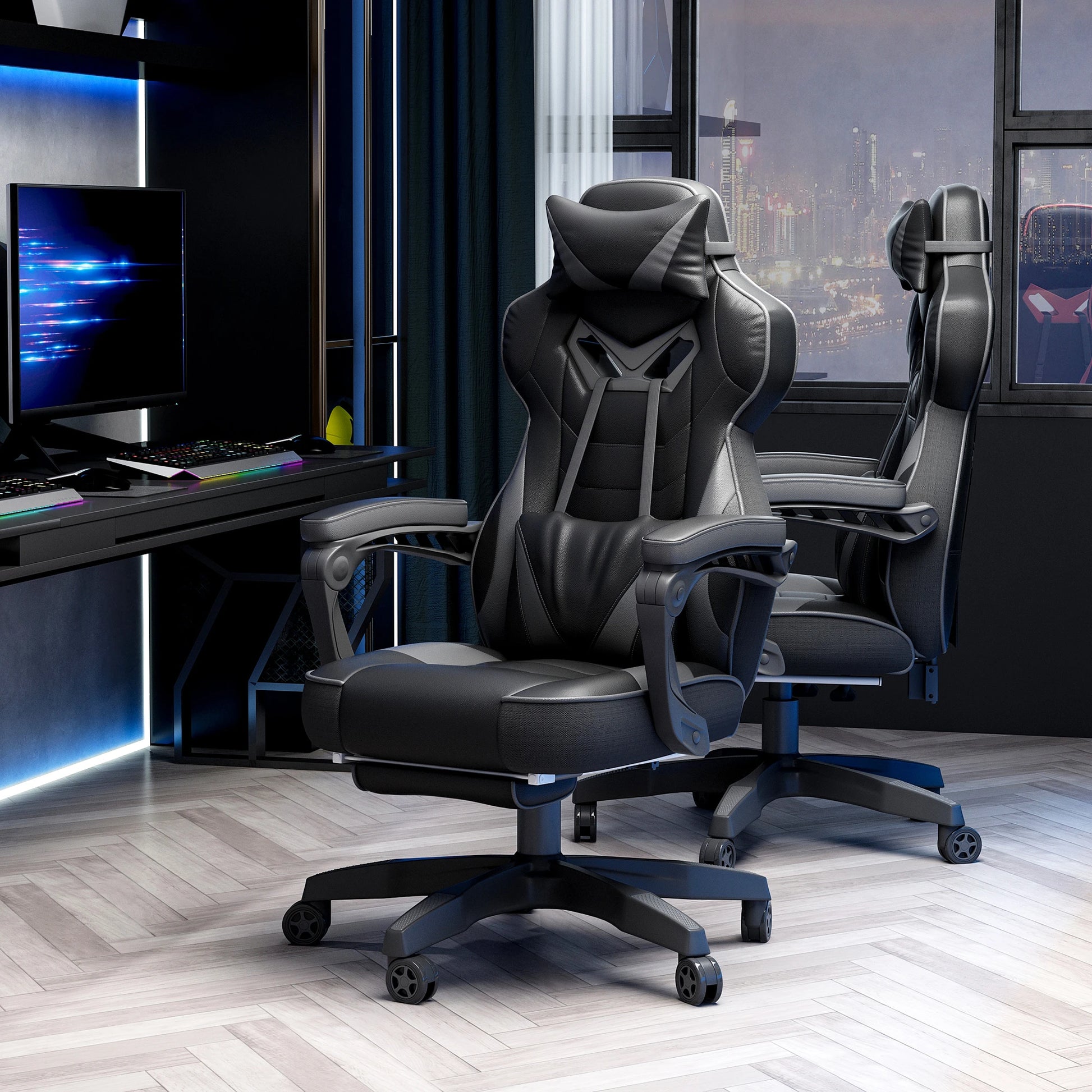 A grey and black computer gaming chair with lumbar support and footrest, positioned in a room with a desk and a view of buildings outside.