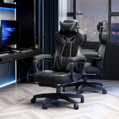 A grey and black computer gaming chair with lumbar support and footrest, positioned in a room with a desk and a view of buildings outside.