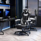 A white and black computer gaming chair with lumbar support and footrest, positioned in a room with a desk and computer setup.