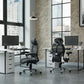 Modern office setup with two ergonomic chairs and desks in a large windowed room.