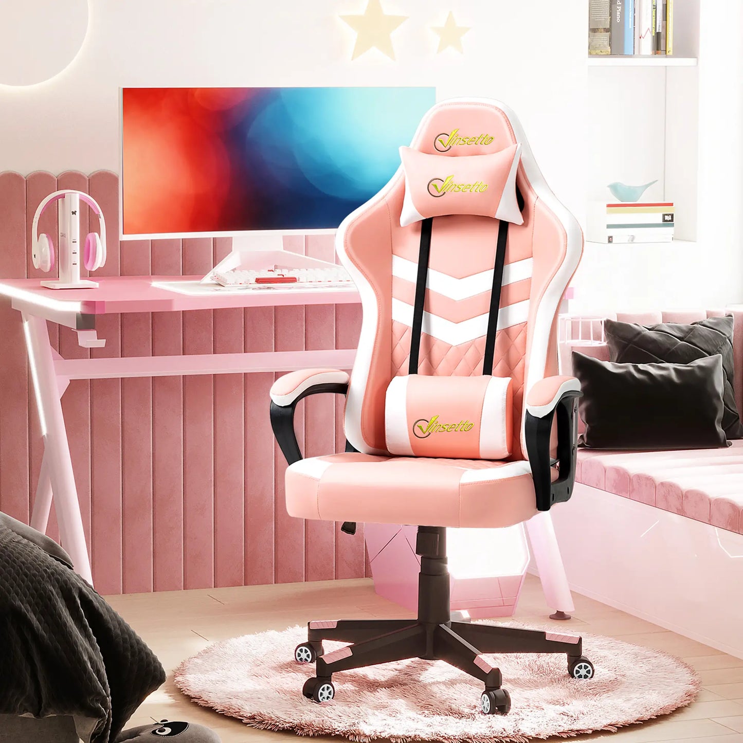 A pink gaming chair with lumbar and headrest support, placed in a room with a computer setup, featuring a large swivel seat and a high backrest.