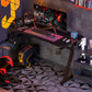 A black gaming desk with a steel frame, featuring a large worktop, a cup holder, and a cable organiser. The desk is in a room with gaming equipment setup.
