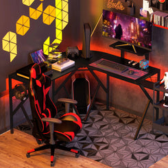 An L-shaped black gaming desk with an adjustable monitor stand, featuring a headphone hook, cup holder, and a carbon fiber texture. It is set in a room with neon lights and a gaming setup.