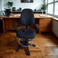 Dark office chair in front of a wooden desk with a laptop and speakers.
