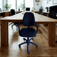 Black office chair in a modern office setting with wooden tables and chairs.