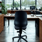 almost black office chair in a modern office setting with large windows.