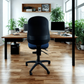Modern office with a black office chair in the foreground and desks with computers in the background.