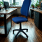 Blue office chair in an office setting with desks and windows.