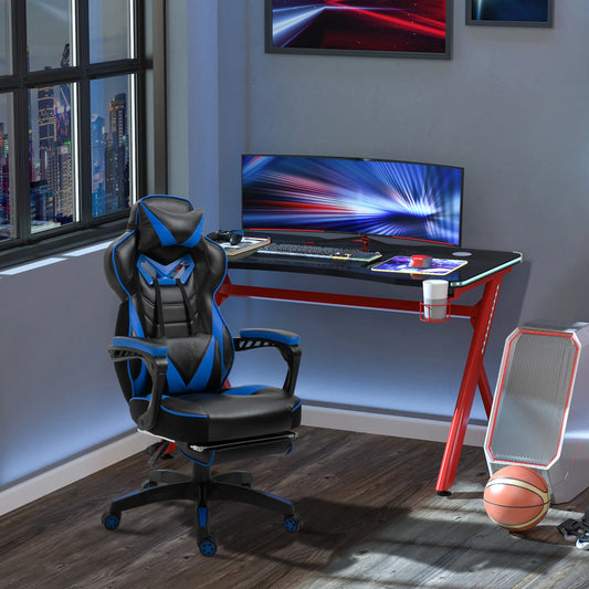 A black and blue gaming chair with thick padding, padded armrests, and a high backrest, situated in a room with a desk and a computer setup in the background.