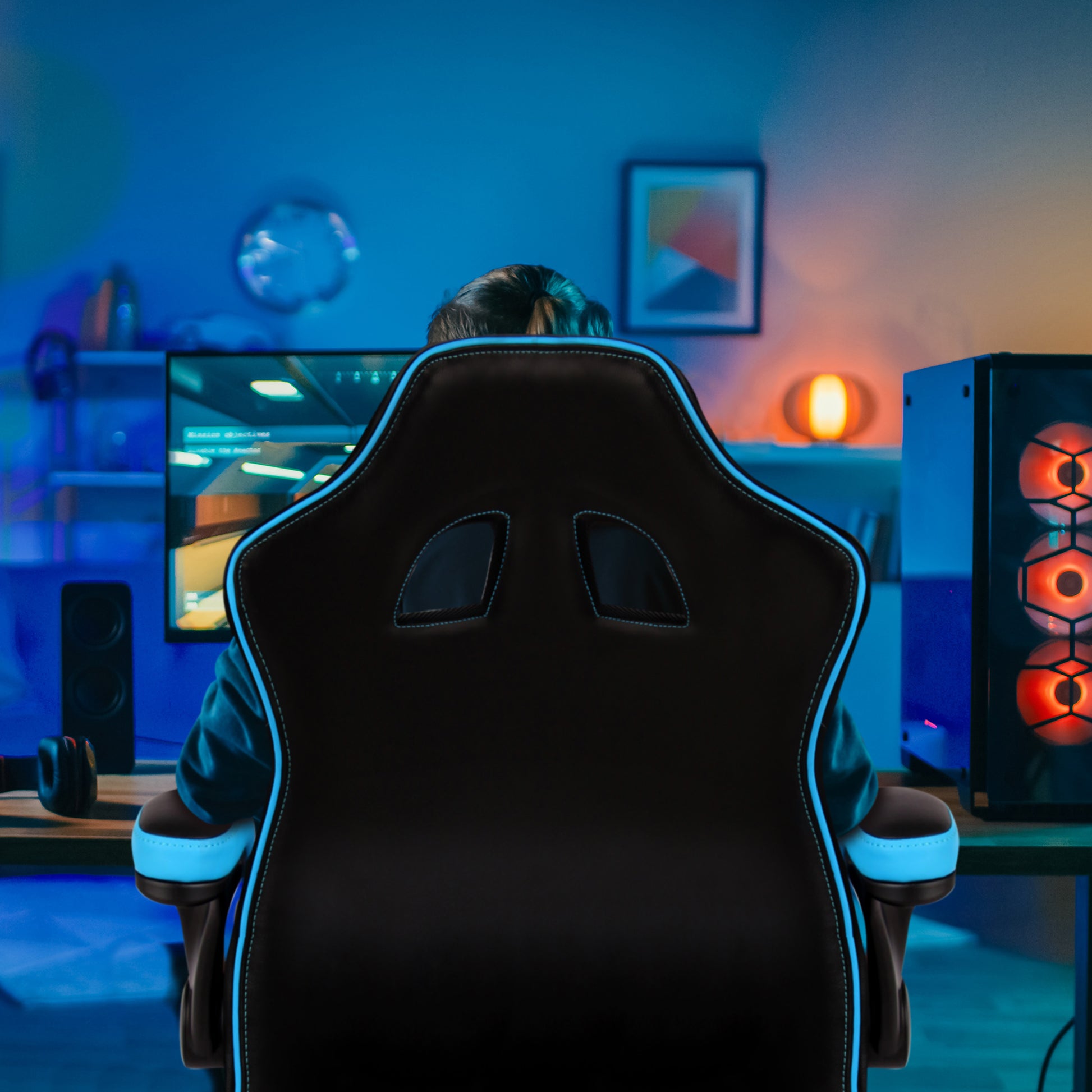 Person sitting in a gaming chair in a room with blue lighting, facing a computer setup.
