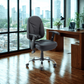 Gray office chair in front of a wooden desk with a cityscape view through large windows.