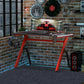 A black and red gaming desk with RGB LED light strips, 'R' leg steel frame, and accessories such as a cup holder and headphone hook.