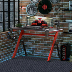 A black and red gaming desk with RGB LED light strips, 'R' leg steel frame, and accessories such as a cup holder and headphone hook.