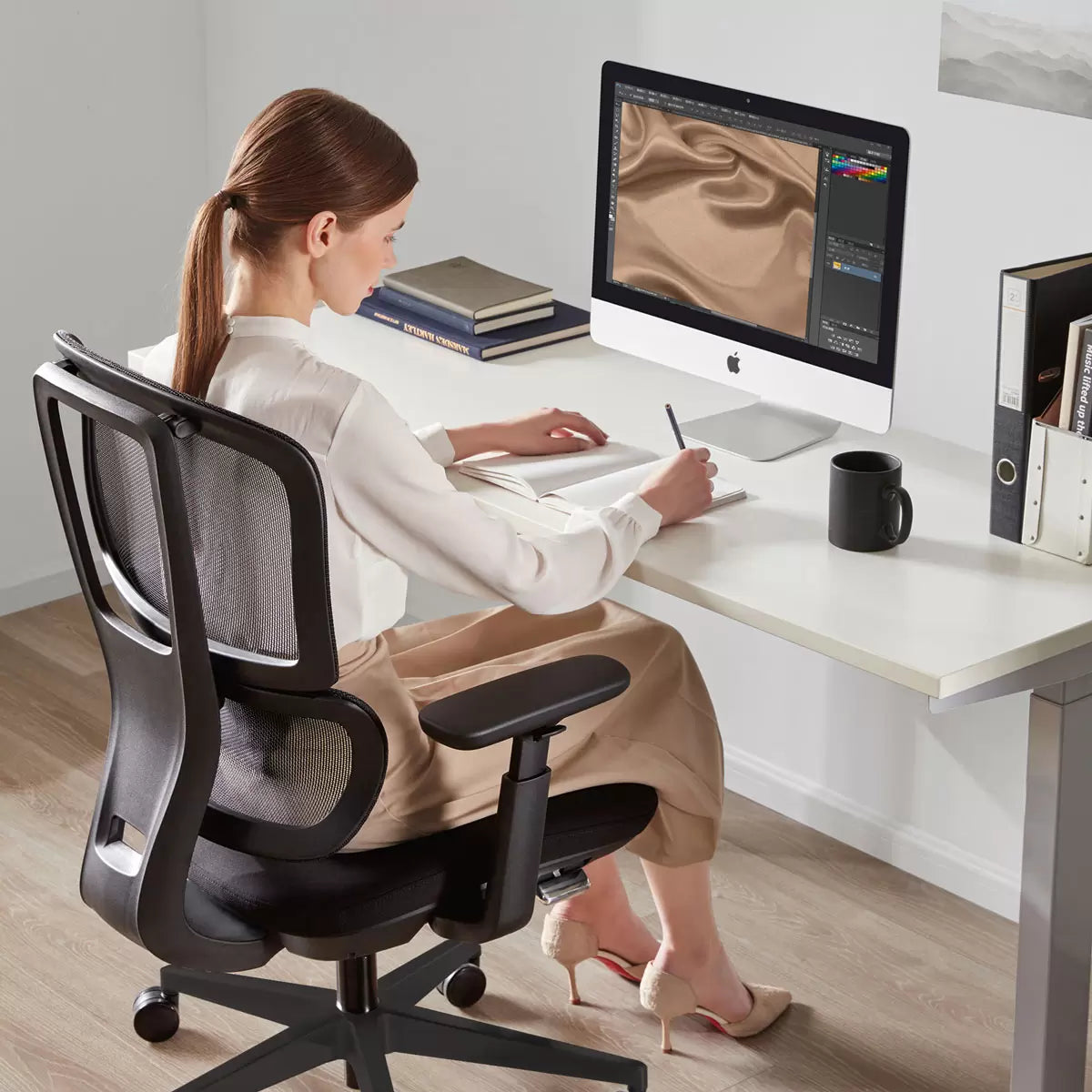 Woman sitting at a desk using a computer with a black office chair.